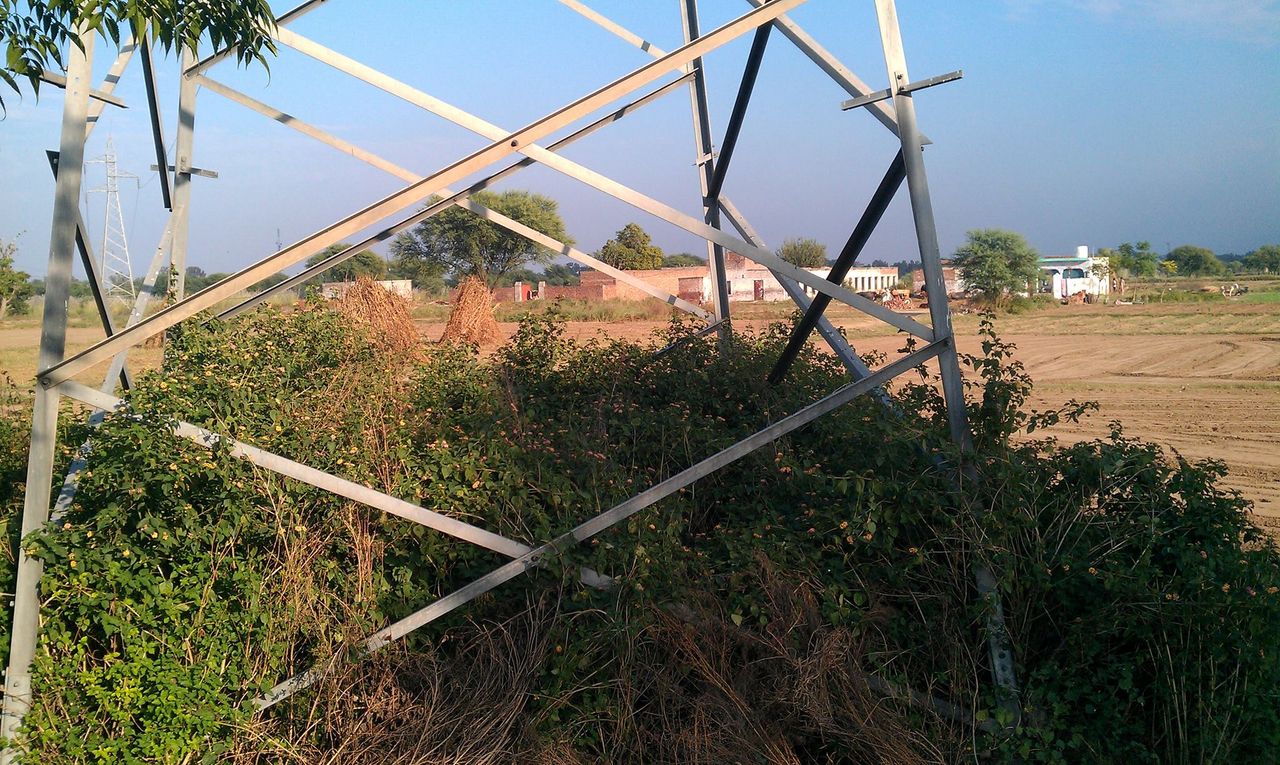 A steel electricity transmission tower carrying overhead power lines across fields near Thathi Mughlan, Jhelum