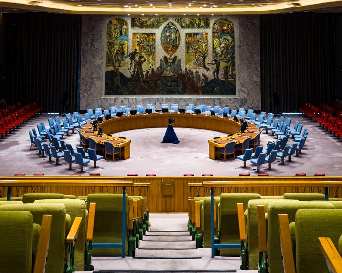 The United Nations Security Council chamber in New York, showing its curving rows of seats and large mural.