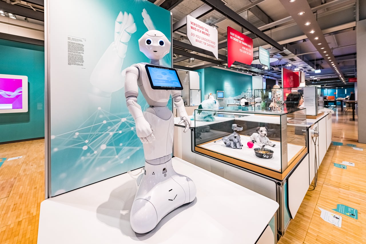 A museum exhibition on artificial intelligence and robotics with illuminated displays and a robotic arm exhibit