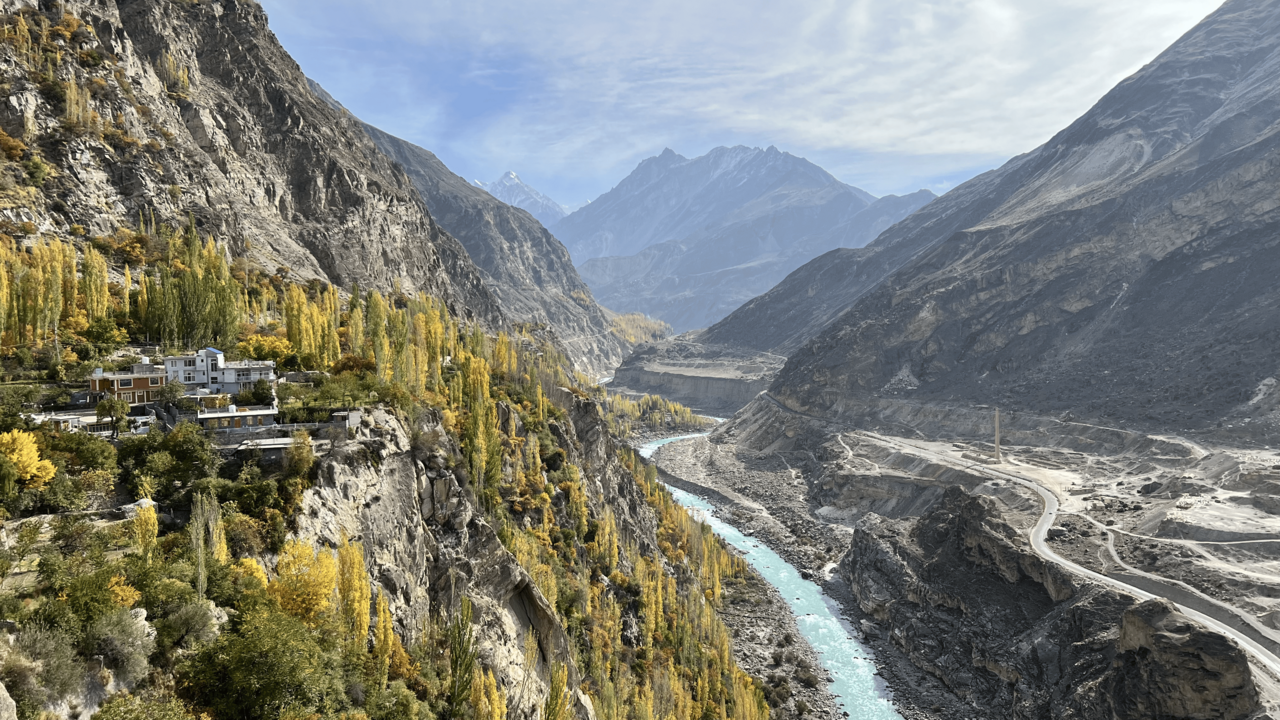 Wide view of the River Indus in autumn, with shallow braided channels across a wide sandy bed flanked by low rocky hills.
