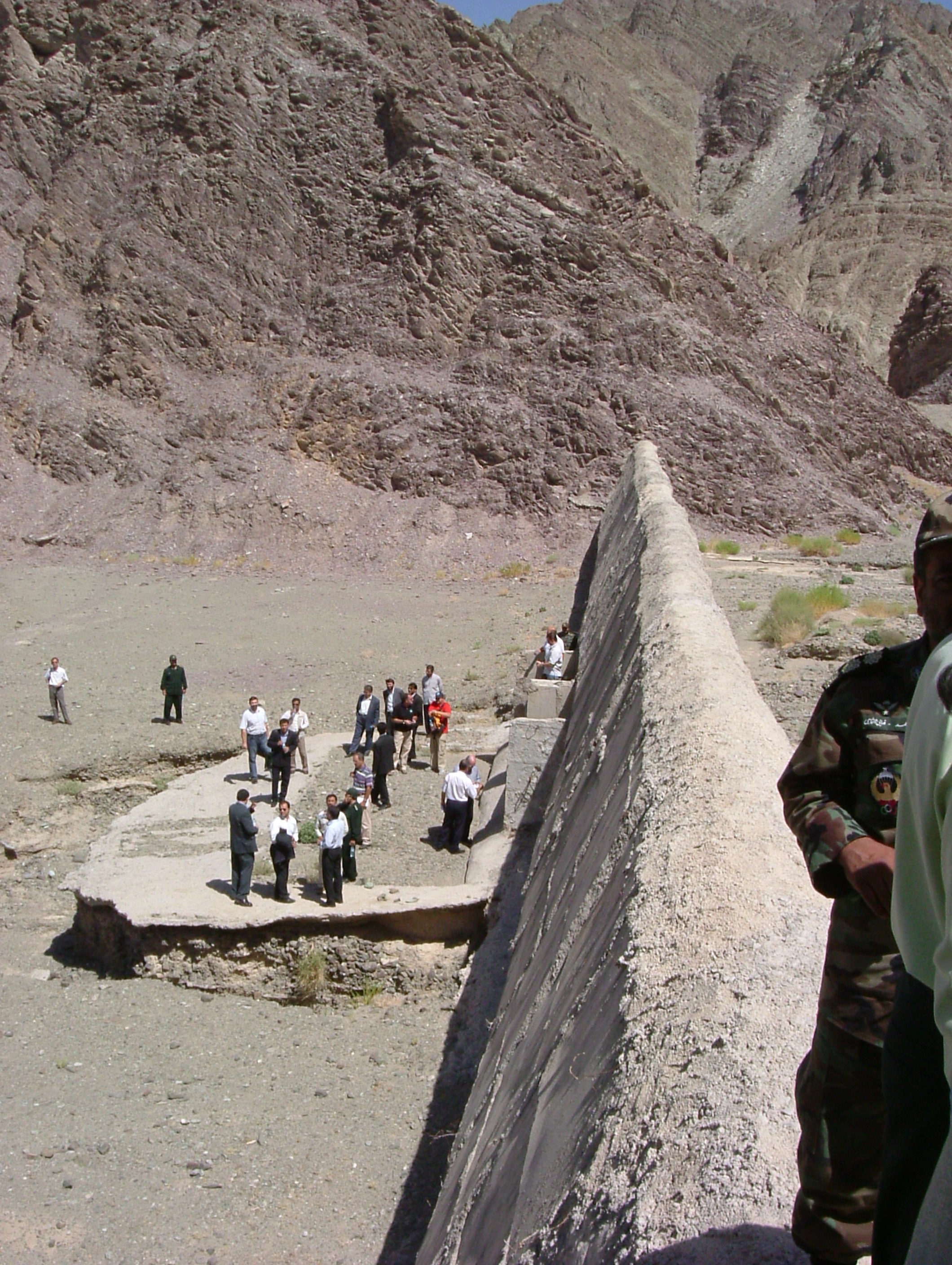 A concrete anti-smuggling barrier stretching into the distance along a dirt track at the Iran-Pakistan border in arid terrain.