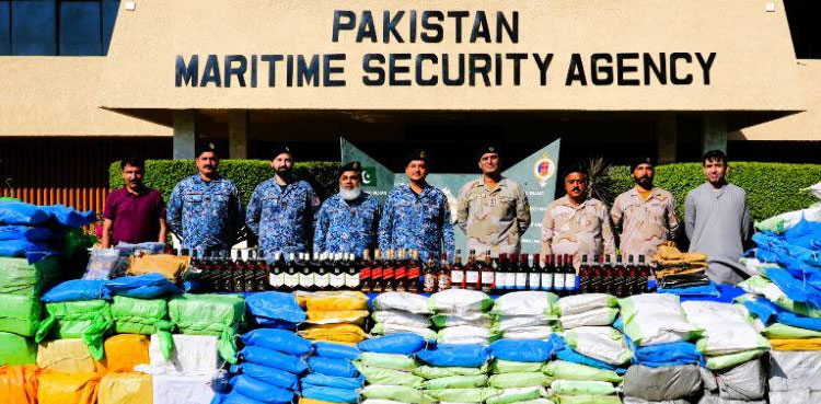 Uniformed Pakistan Maritime Security Agency personnel stand behind rows of colour-coded sacks of seized narcotics and bottles of liquor laid out in front of an agency building.