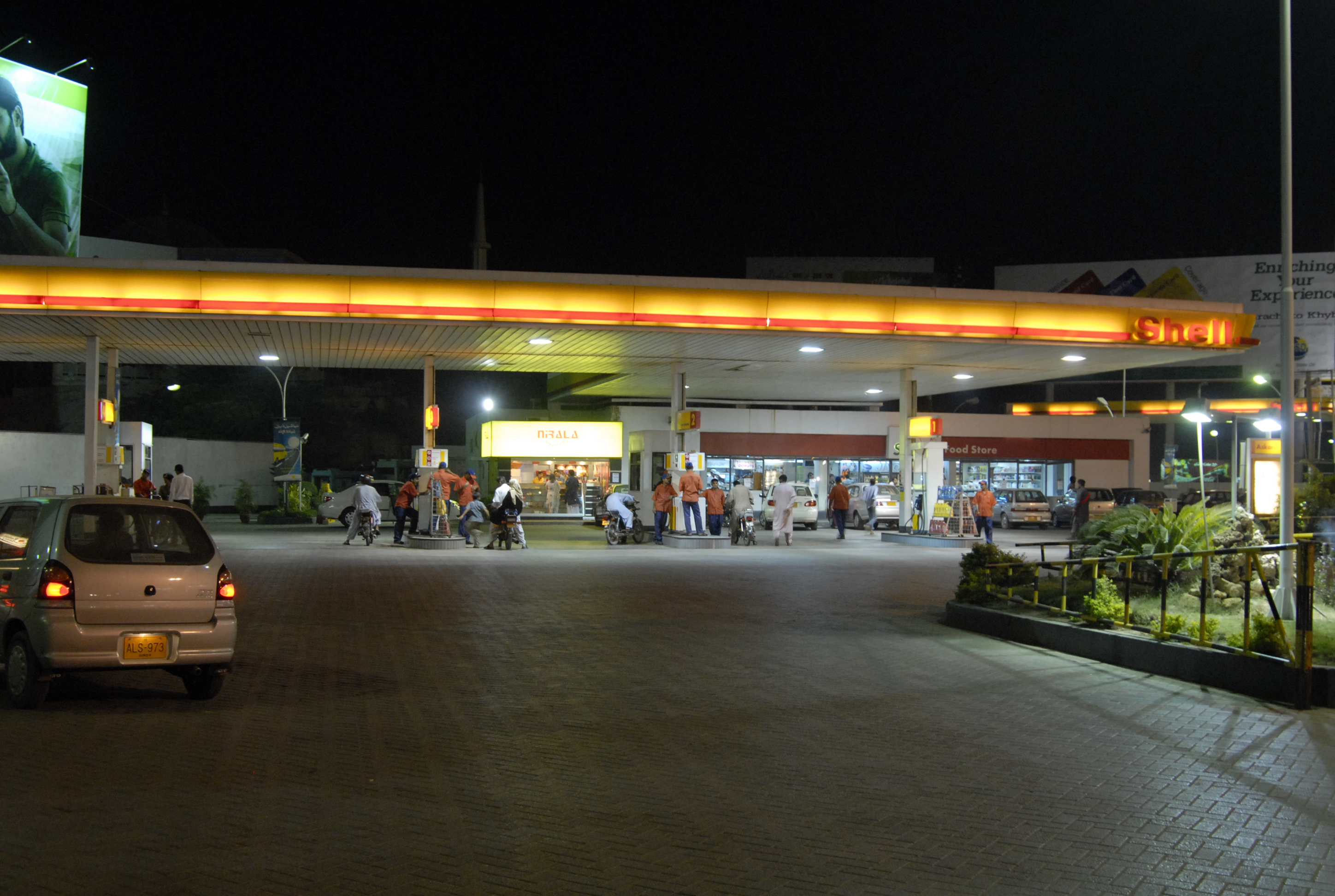 A Shell fuel station forecourt in Karachi at night, with an illuminated canopy over the pumps.