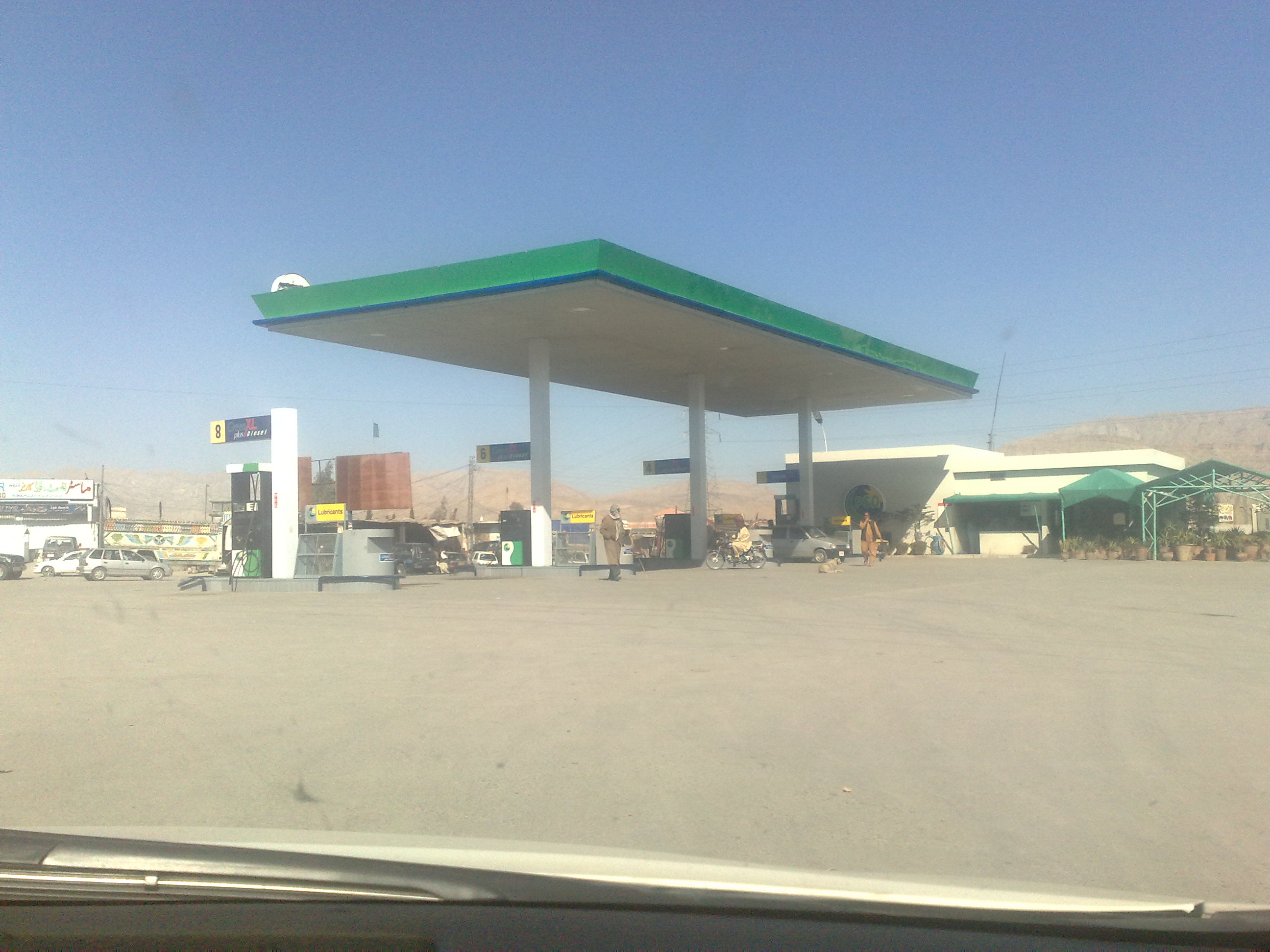 A roadside fuel station with a petrol pump canopy in Khuzdar, Balochistan, with a fuel truck and vehicles parked nearby.