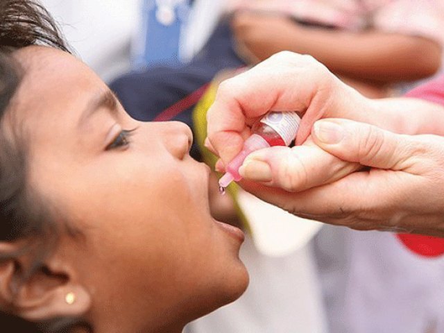 A young child opens their mouth to receive two drops of oral polio vaccine from a health worker's dropper during a vaccination drive