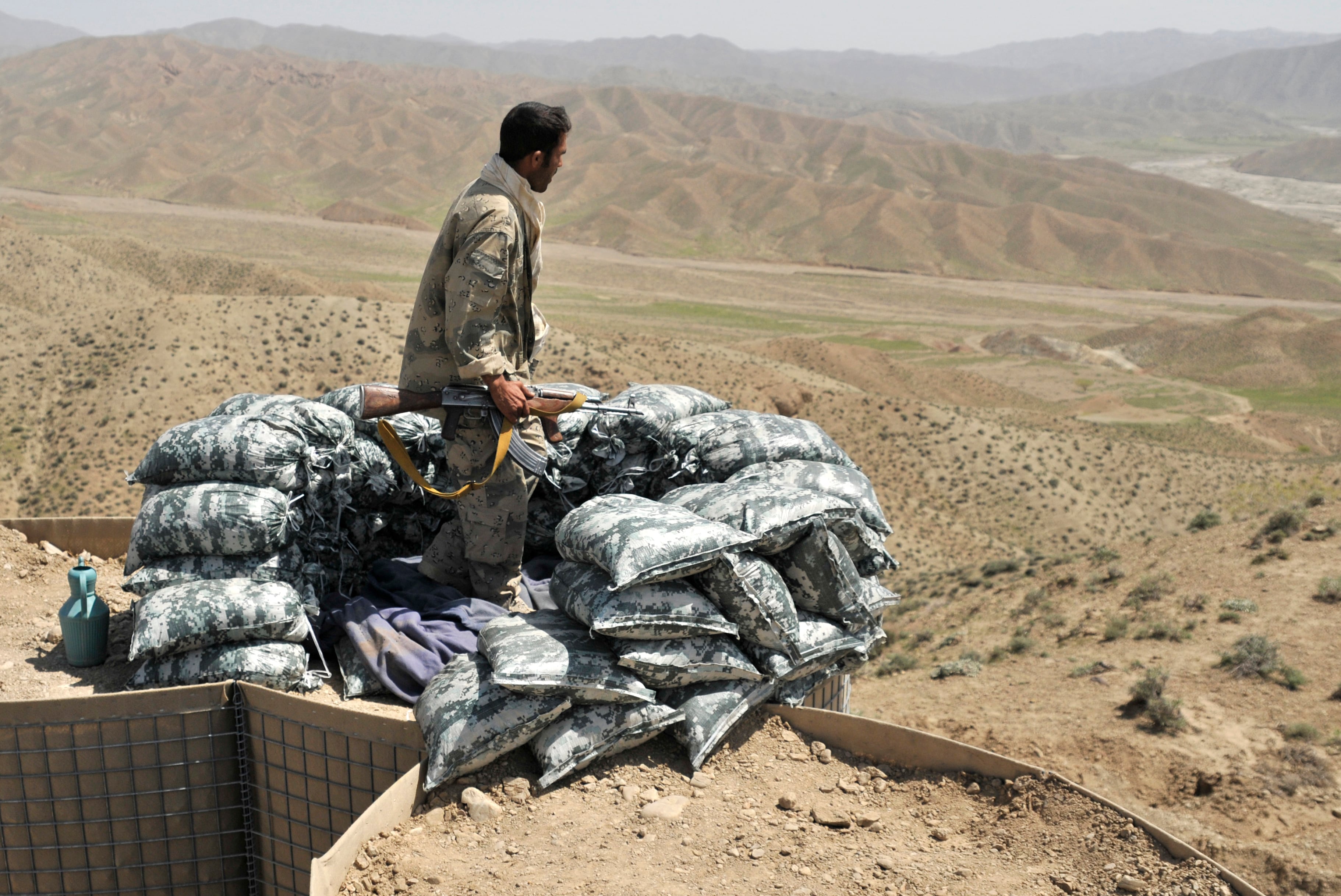 An Afghan border policeman stands beside a newly built checkpoint on a dirt track in arid, mountainous ground near the Pakistan-Afghanistan border.