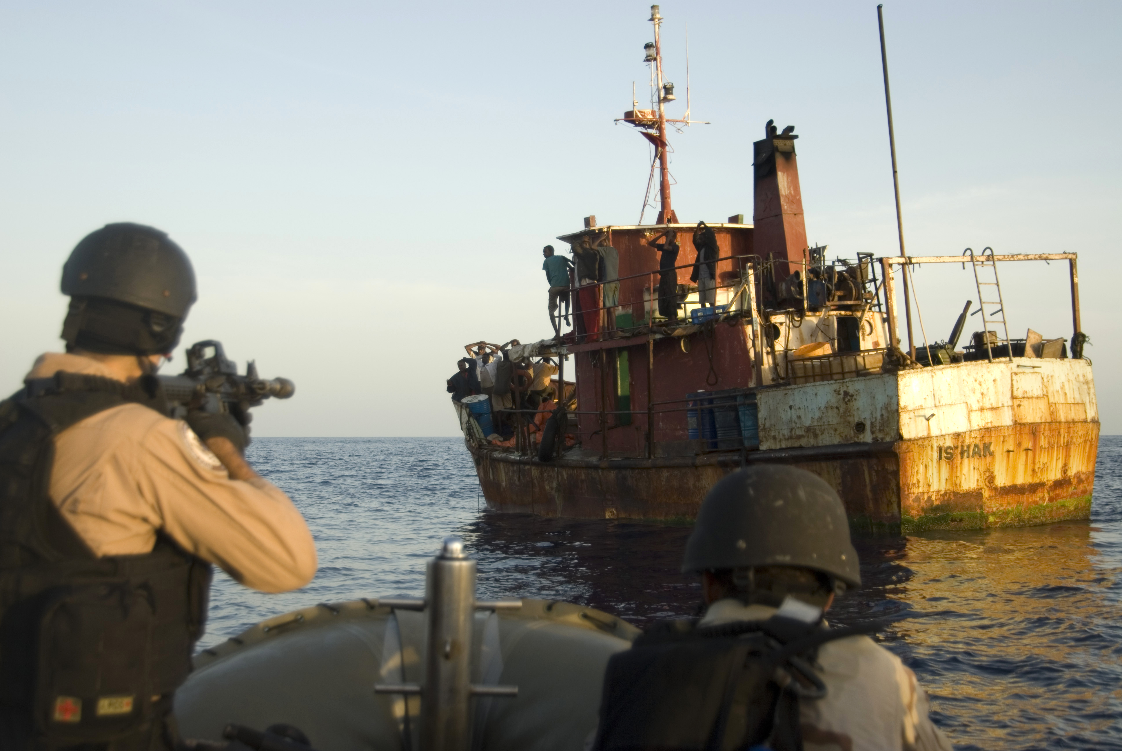 Armed personnel in helmets and tactical vests apprehend suspects on the deck of a vessel during a counter-piracy boarding in the Gulf of Aden