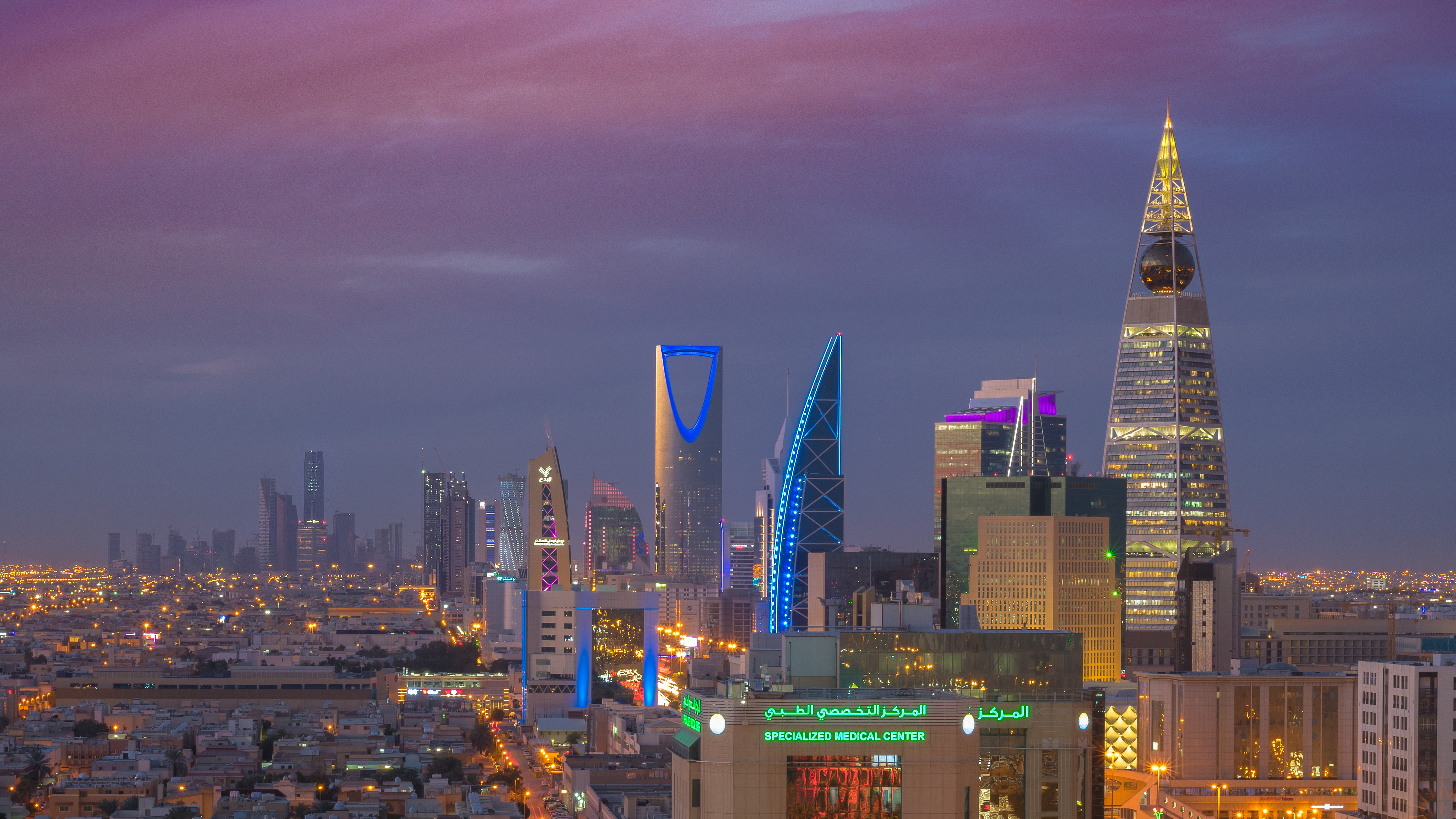 The illuminated Riyadh skyline at night, with the Kingdom Centre tower prominent among high-rise buildings