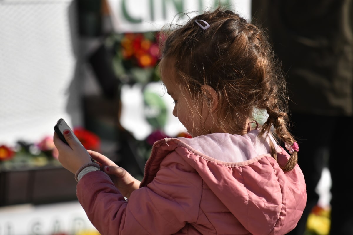 A young girl holding a smartphone and looking down at its screen