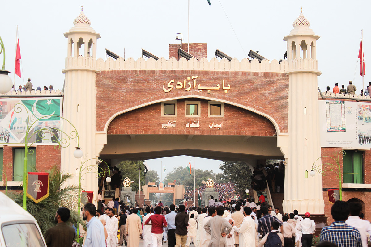 The pale stone Bab-e-Azadi gateway at the Wagah border crossing near Lahore, with its arched facade, flag and an approach road to the crossing