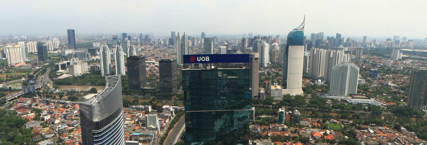 Panoramic view of the Jakarta city skyline seen from the Grand Indonesia area, with high-rise towers along a wide thoroughfare under a partly cloudy sky.