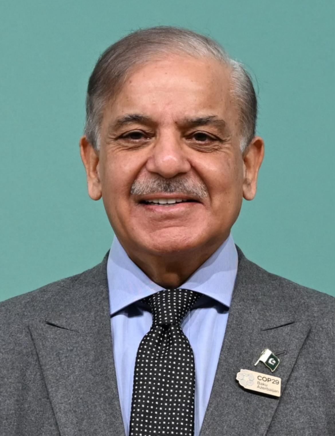 Prime Minister Shehbaz Sharif standing in a hall in formal attire during an international summit, used here to illustrate the leader of Pakistan.
