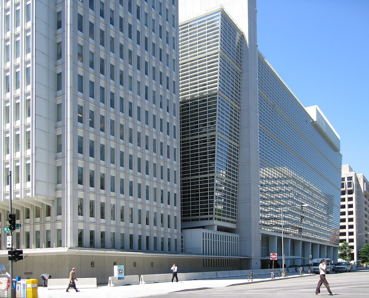 The granite and glass World Bank Group headquarters building in Washington, D.C., viewed from Pennsylvania Avenue, with its lower colonnade visible behind a low stone wall.