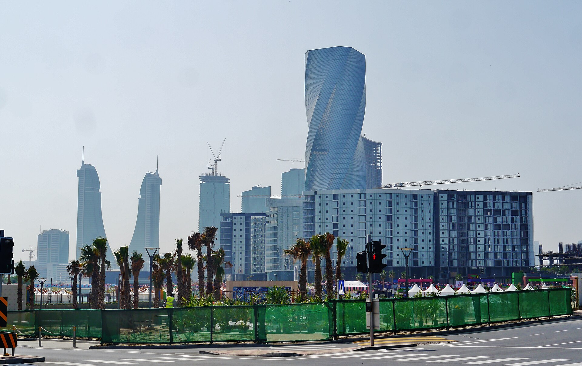 The Manama skyline in Bahrain, showing glass high-rises, palm trees and a waterfront road.