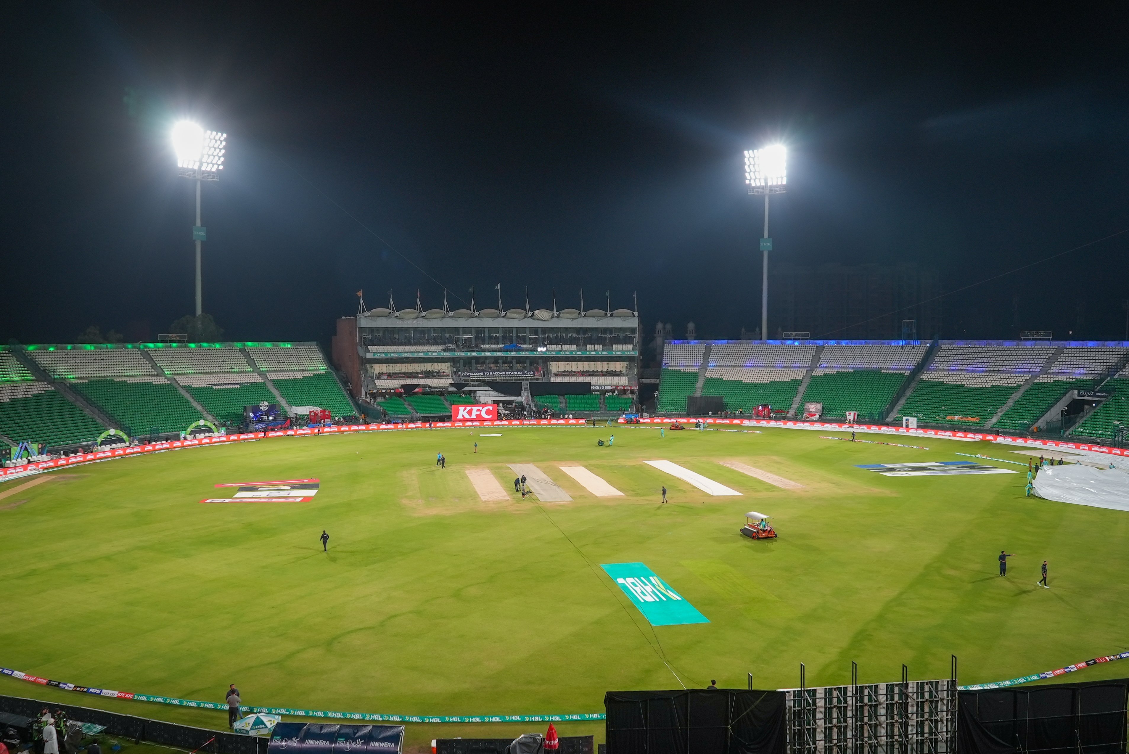 Wide view of the floodlit Gaddafi Stadium in Lahore during a Pakistan Super League fixture, with the green outfield, advertising boards and stadium seating visible