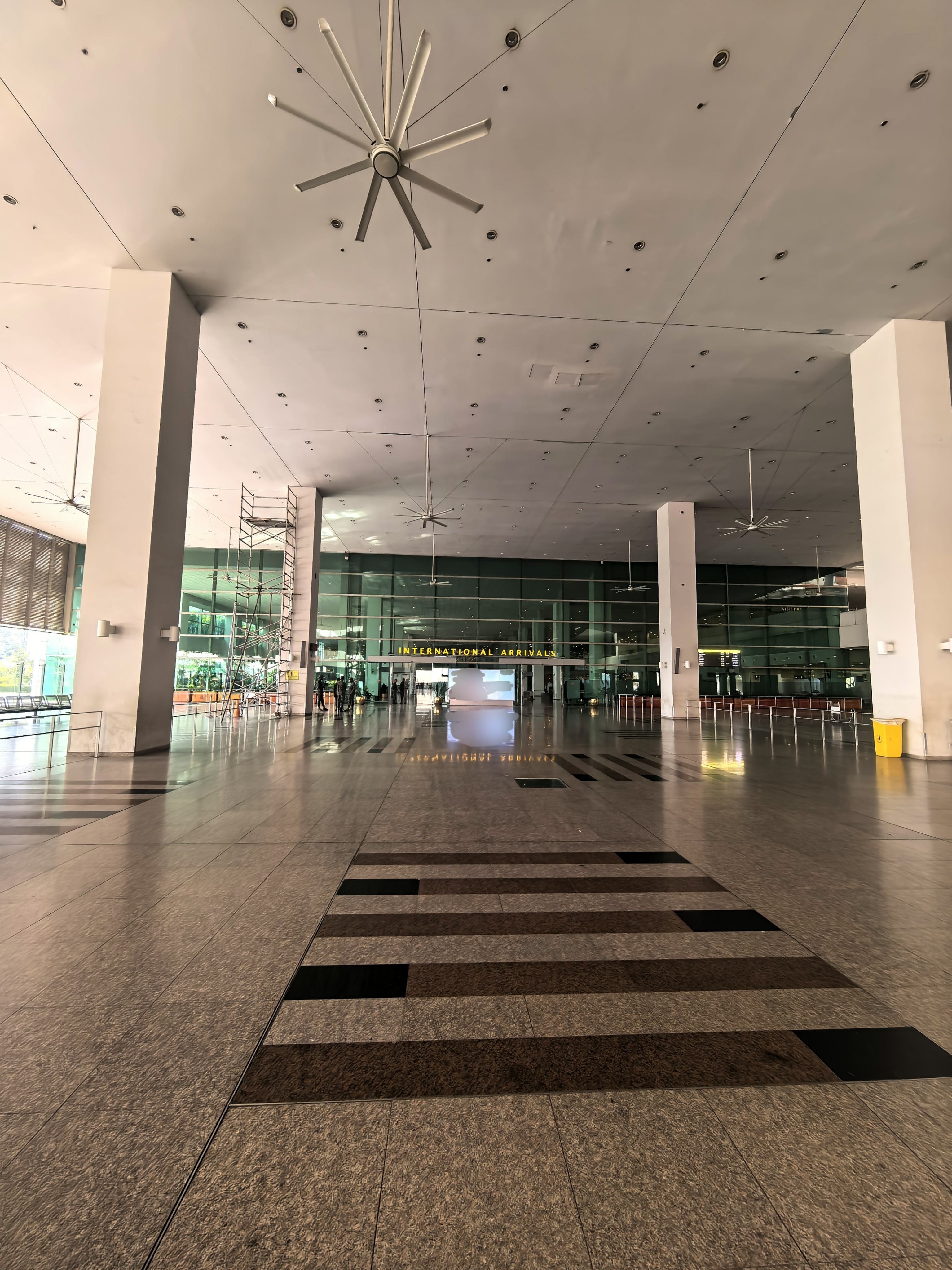 Wide-angle view of the international arrivals hall at Islamabad International Airport, showing the entrance signage and the check-in area with travellers and seating.