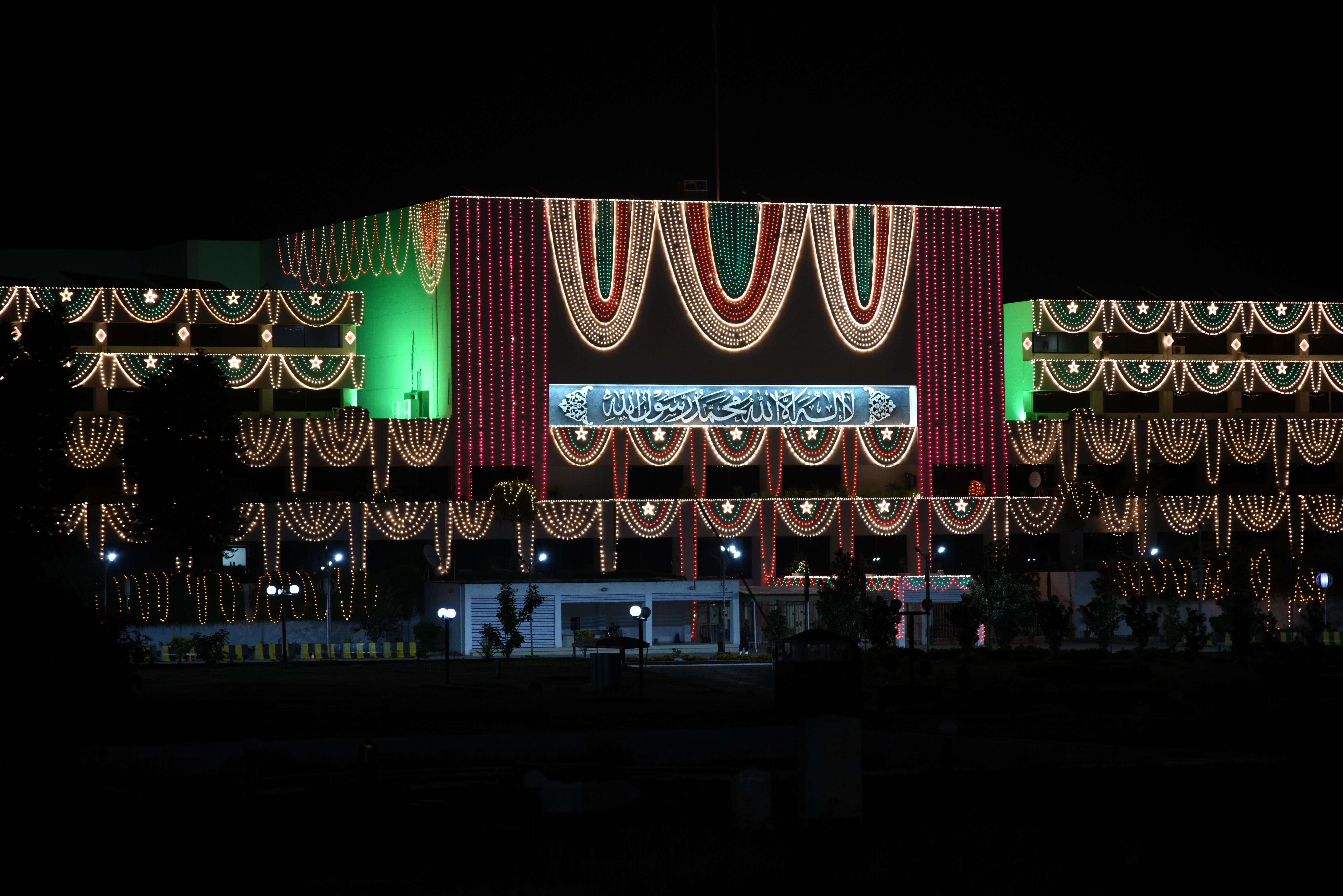Parliament House in Islamabad illuminated at night, with the flag-draped entrance visible