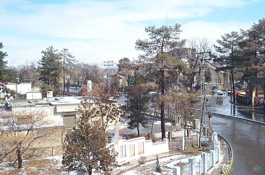 A view of Jinnah Road in Quetta after a snowfall, with cars and shops along a wide central boulevard and low mountains in the background