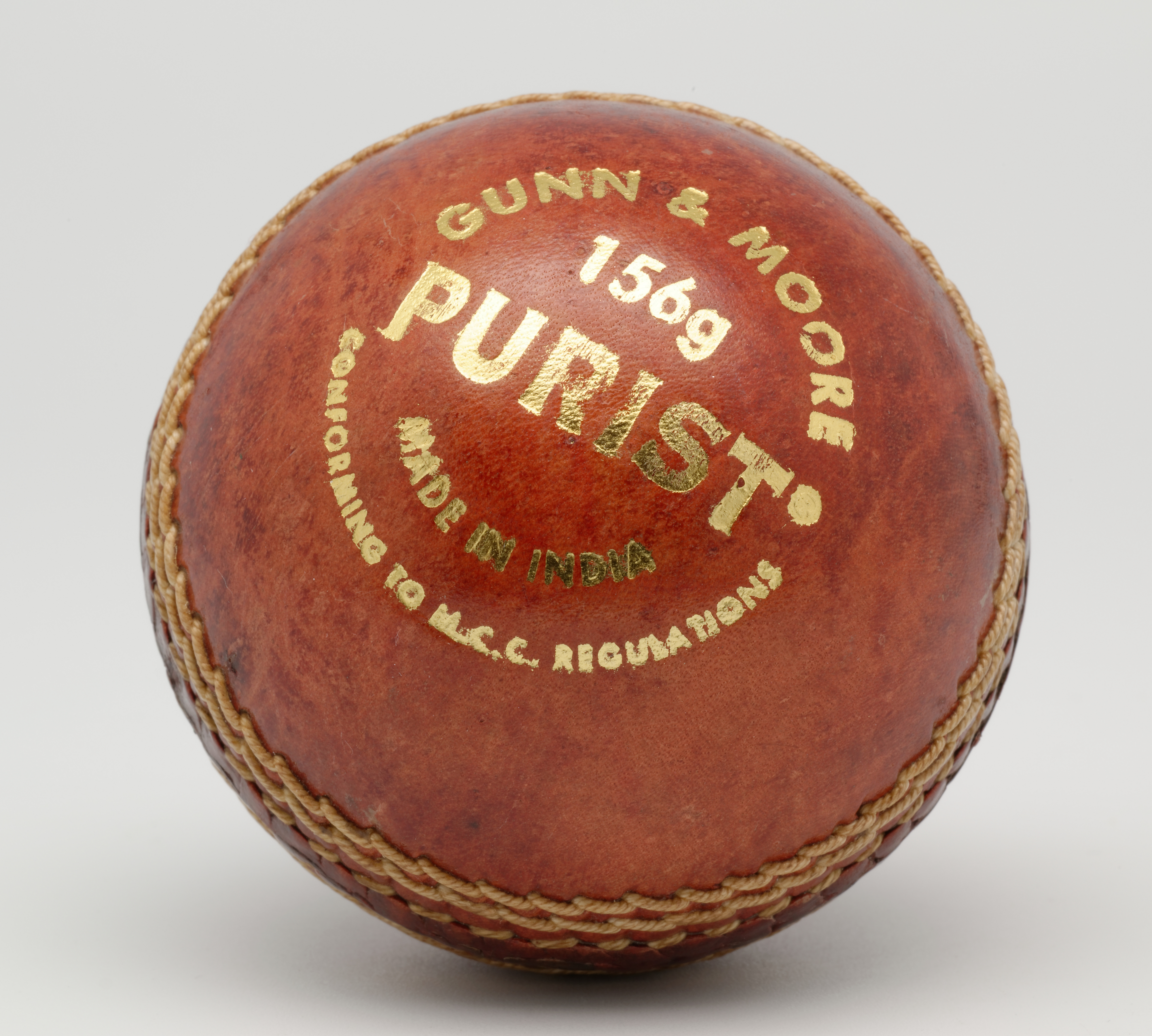 A close-up of a red leather cricket ball with its stitched seam.