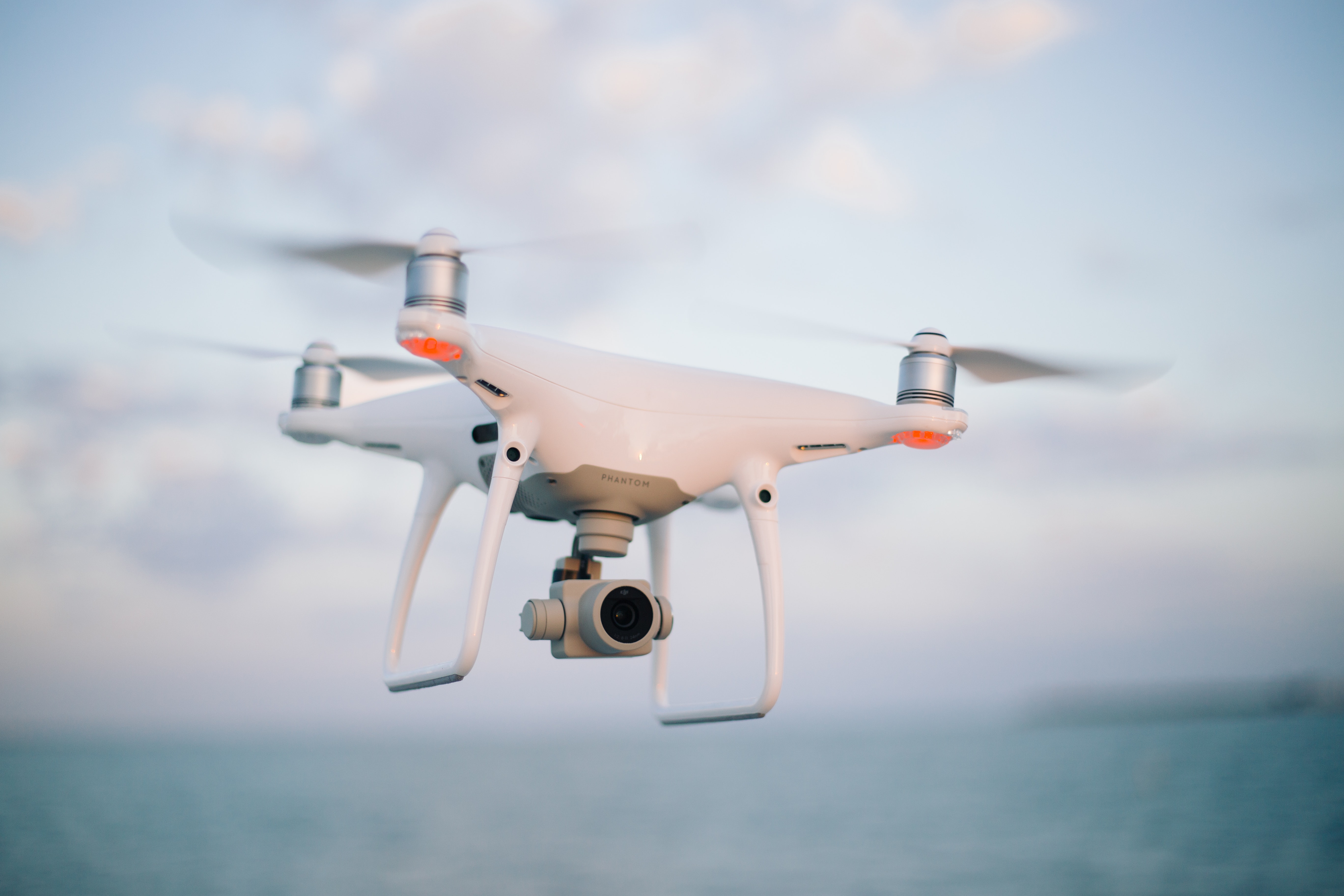 A white camera quadcopter drone with four rotors hovering in a clear sky above a green field
