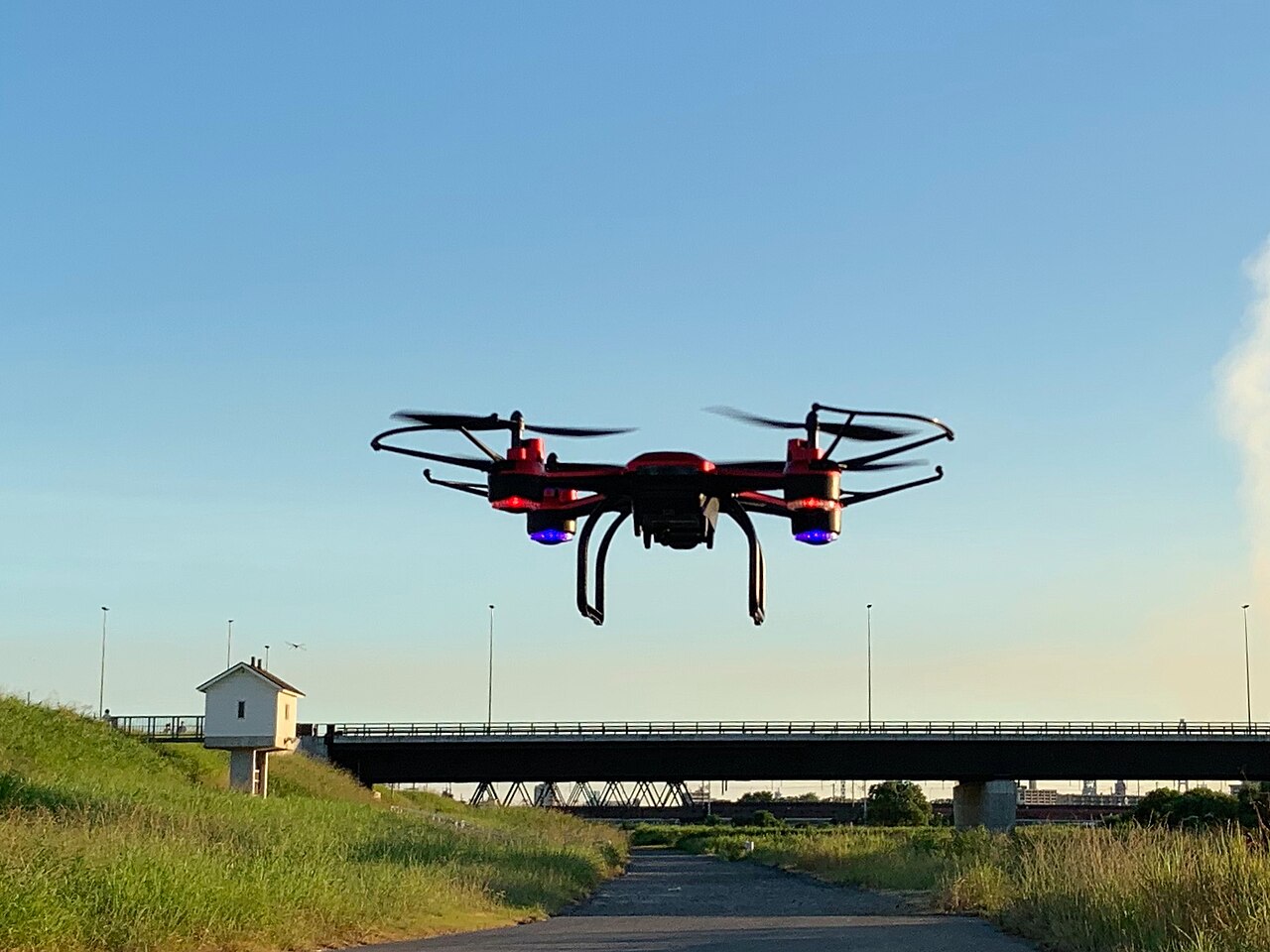 A quadcopter drone hovering against a clear blue sky