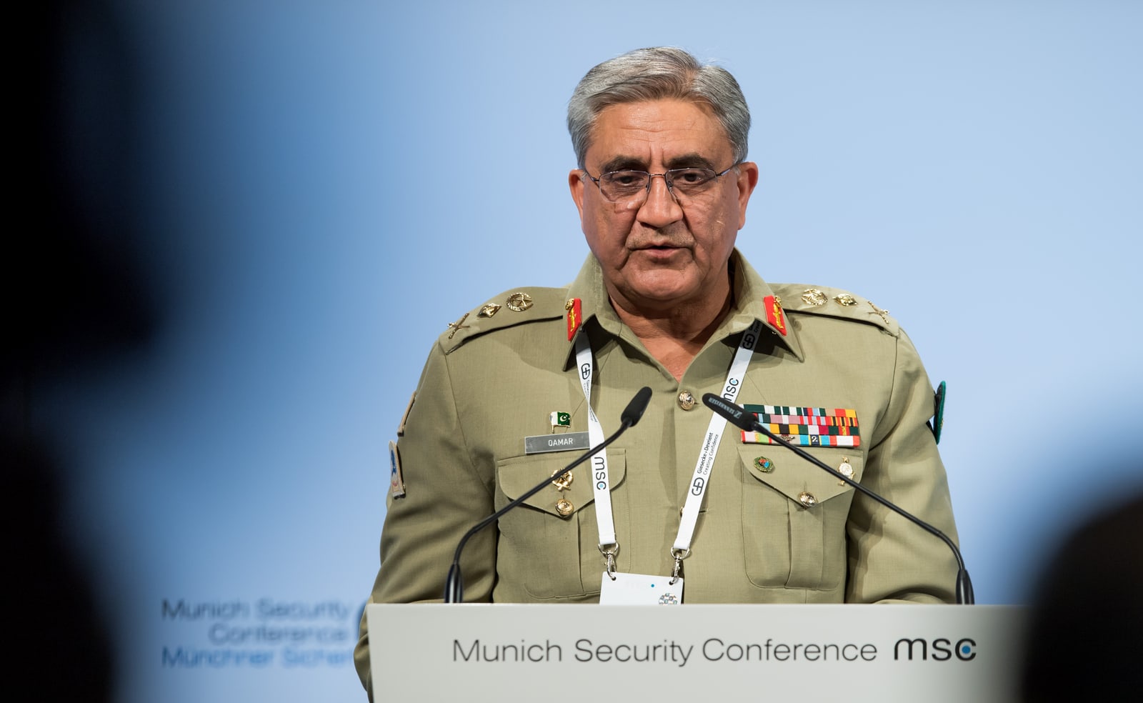 A man in a dark suit and tie speaking at a conference podium