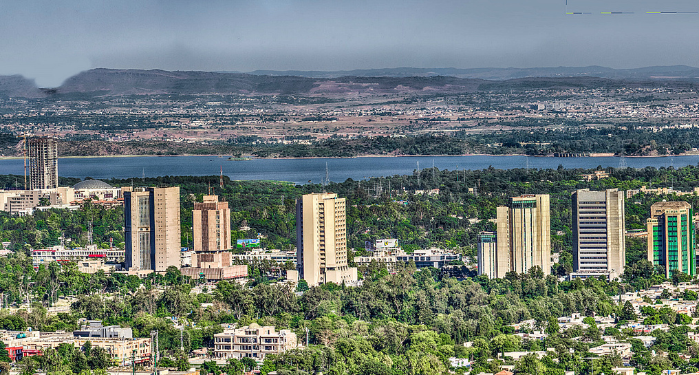 A wide view of Islamabad's cityscape with low buildings and hills under a pale sky.