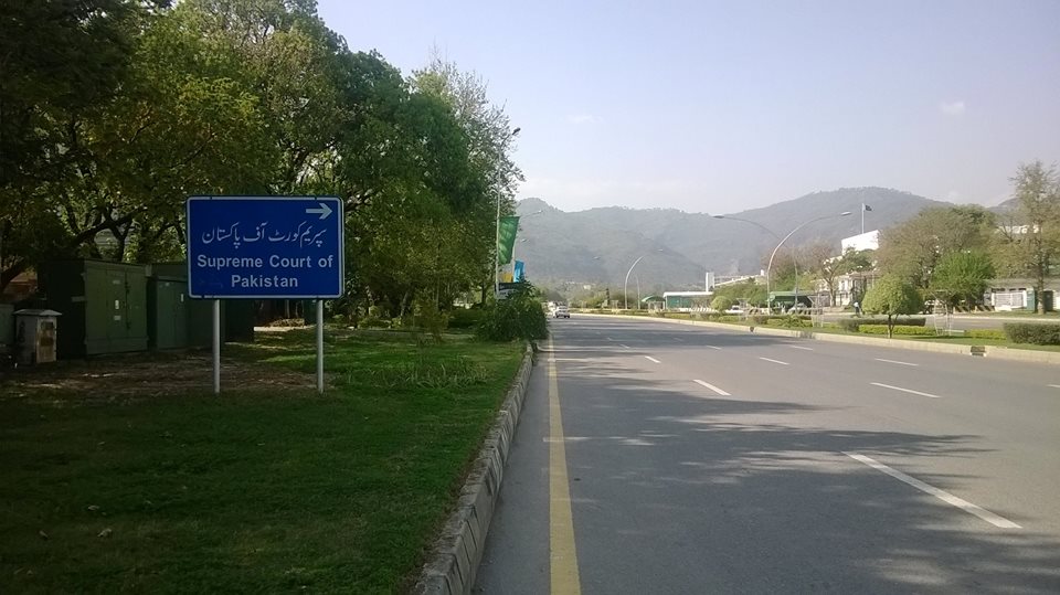 A wide avenue in Islamabad lined with lamp posts and government buildings under a clear sky.