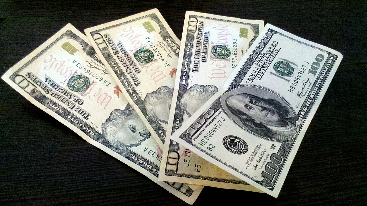 A fan of US dollar banknotes resting on a surface, with $100 and smaller denominations visible