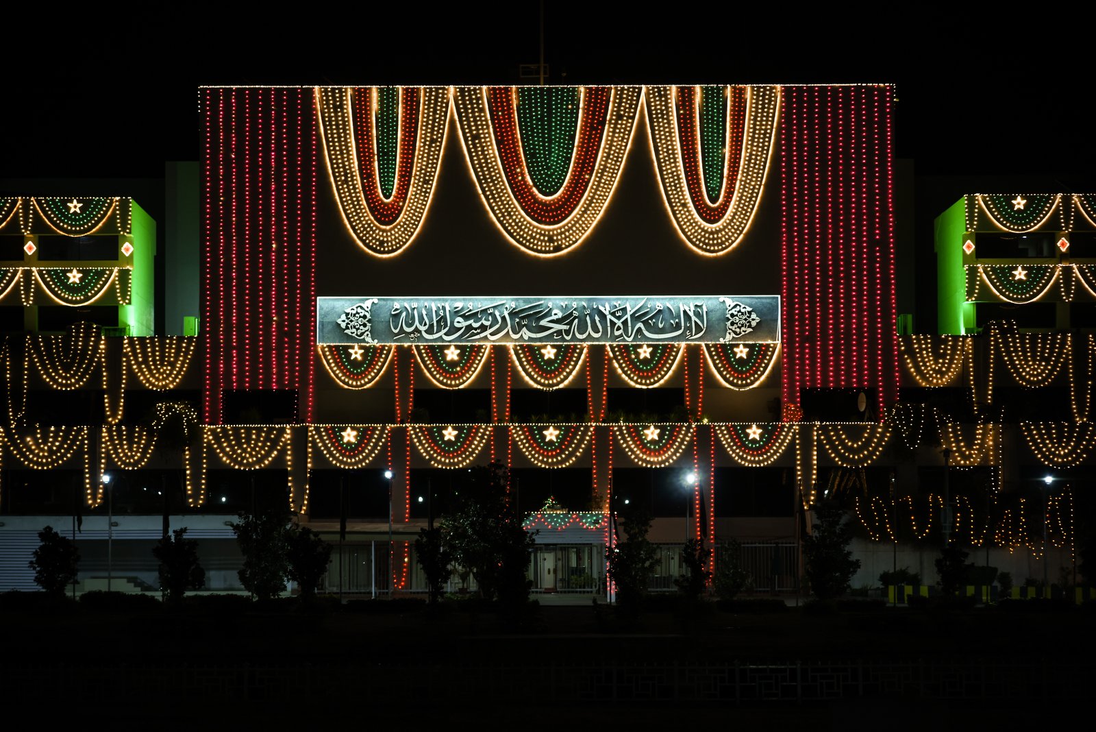A large illuminated modern building with a distinctive roofline photographed at night