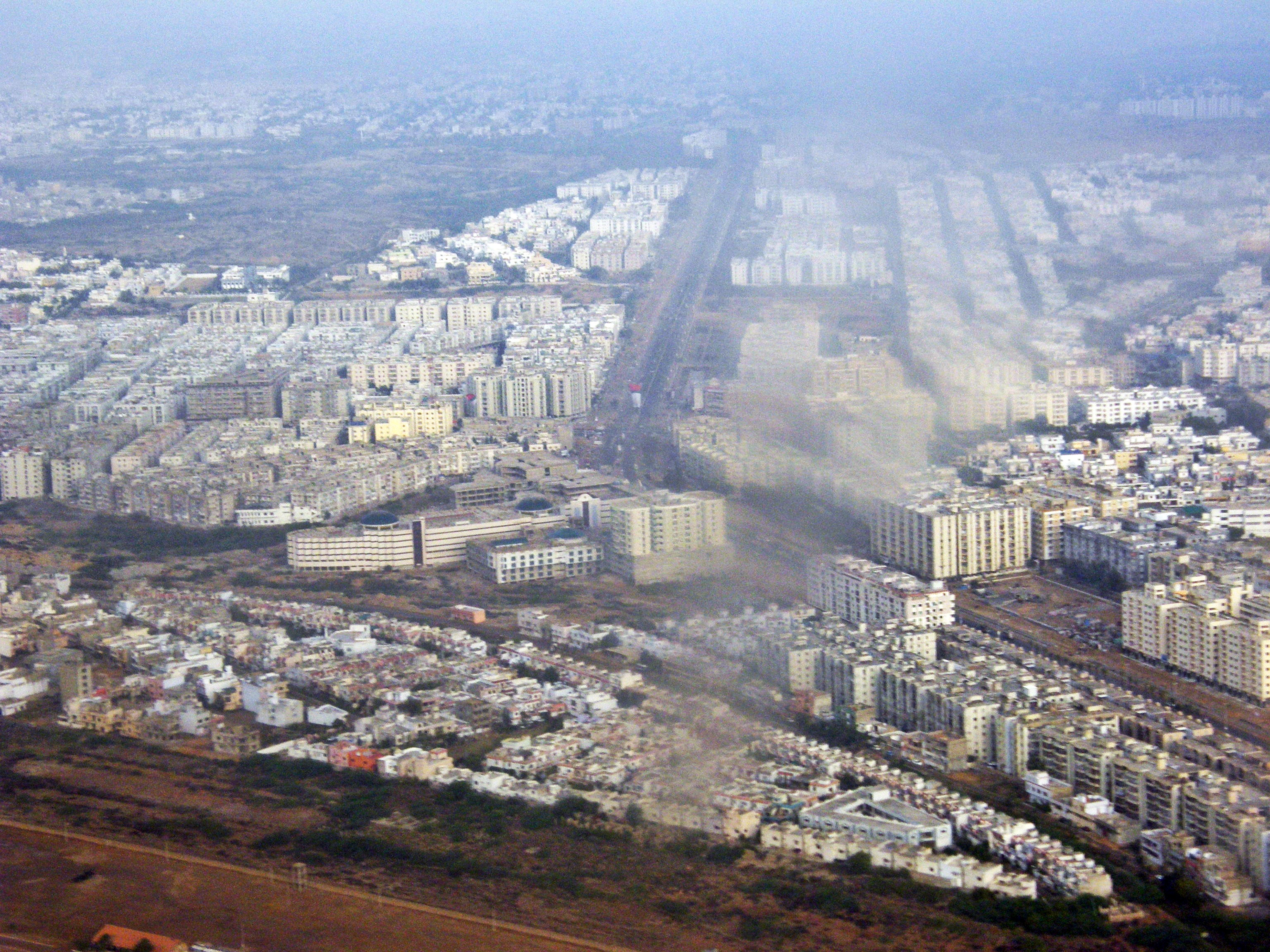 A wide view of Karachi's dense cityscape, with high-rise buildings rising above low-rise neighbourhoods and roads under a hazy sky.