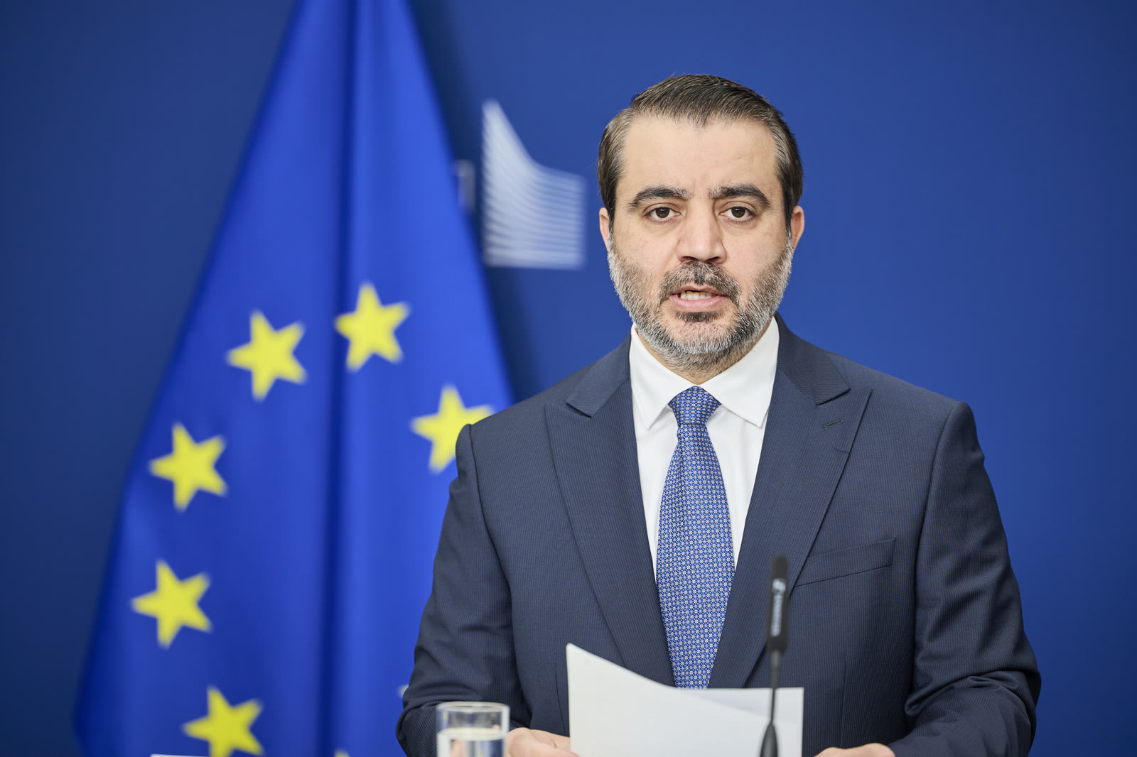 Syrian Foreign Minister Asaad al-Shaibani speaking at a podium during a European Commission event in Brussels.