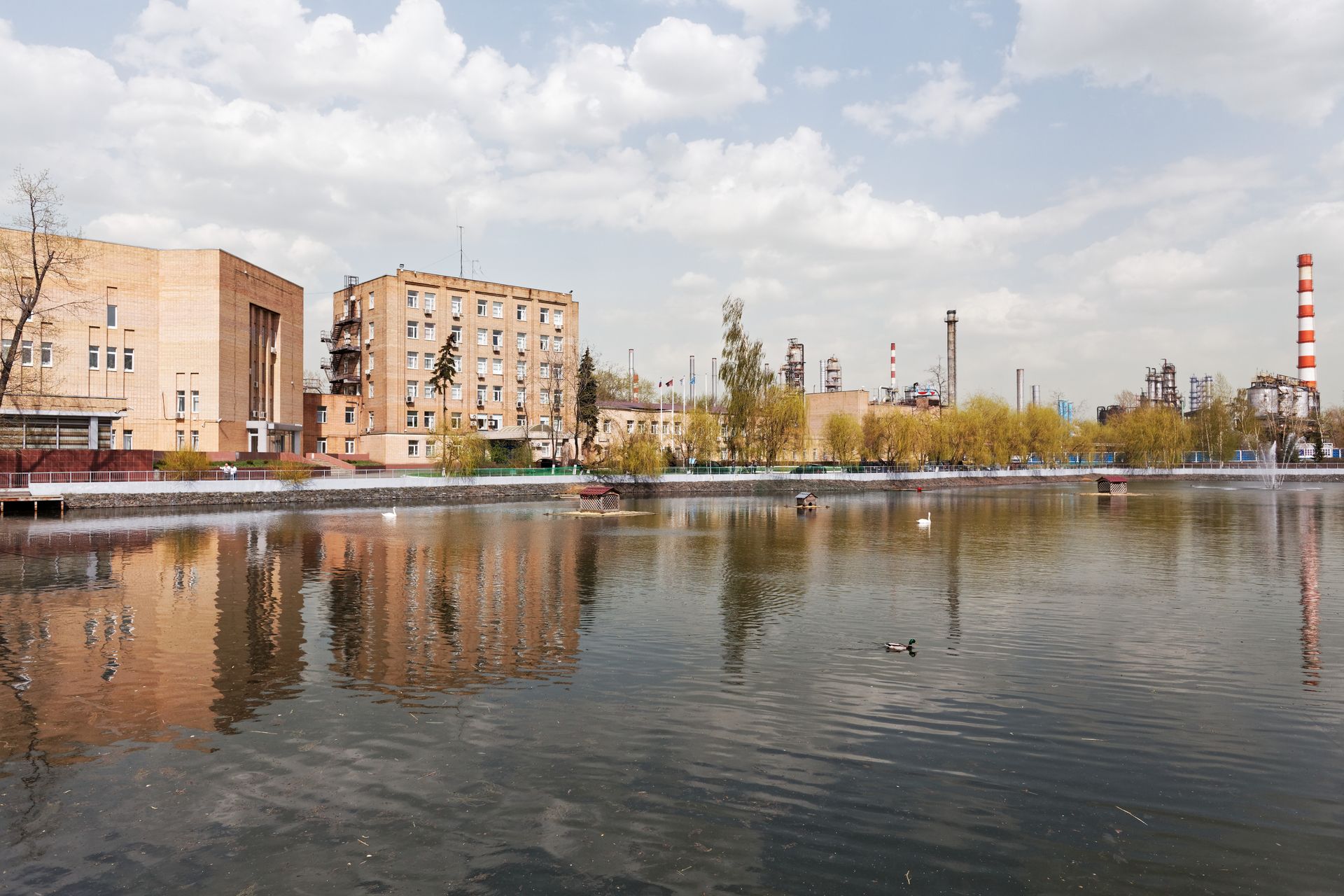 Industrial stacks and process units of the Moscow Oil Refinery in the Kapotnya district, seen across a factory pond