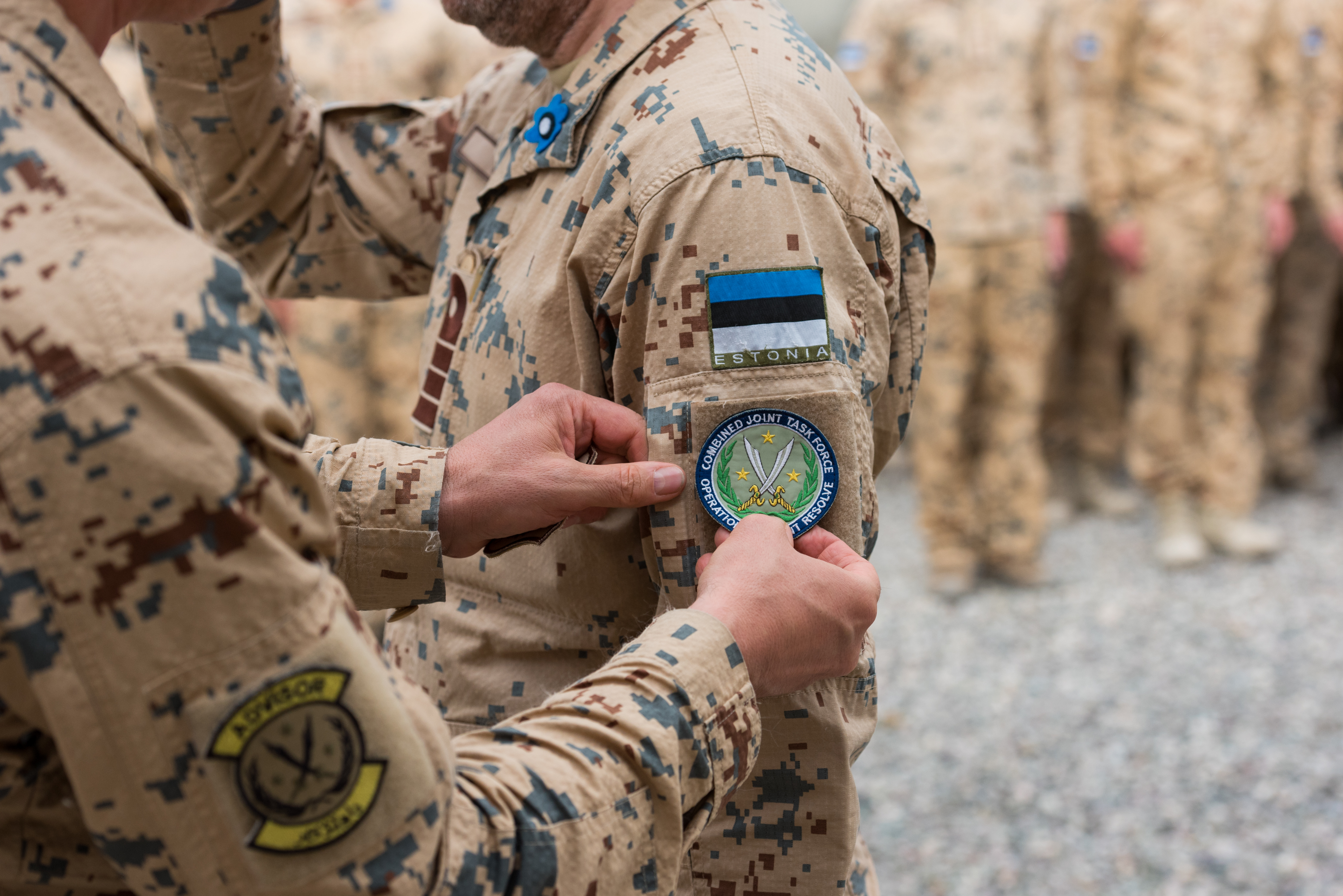 Two soldiers in camouflage uniform stand outdoors as one attaches a Combined Joint Task Force - Operation Inherent Resolve patch to the other's uniform during a ceremony in Iraq.