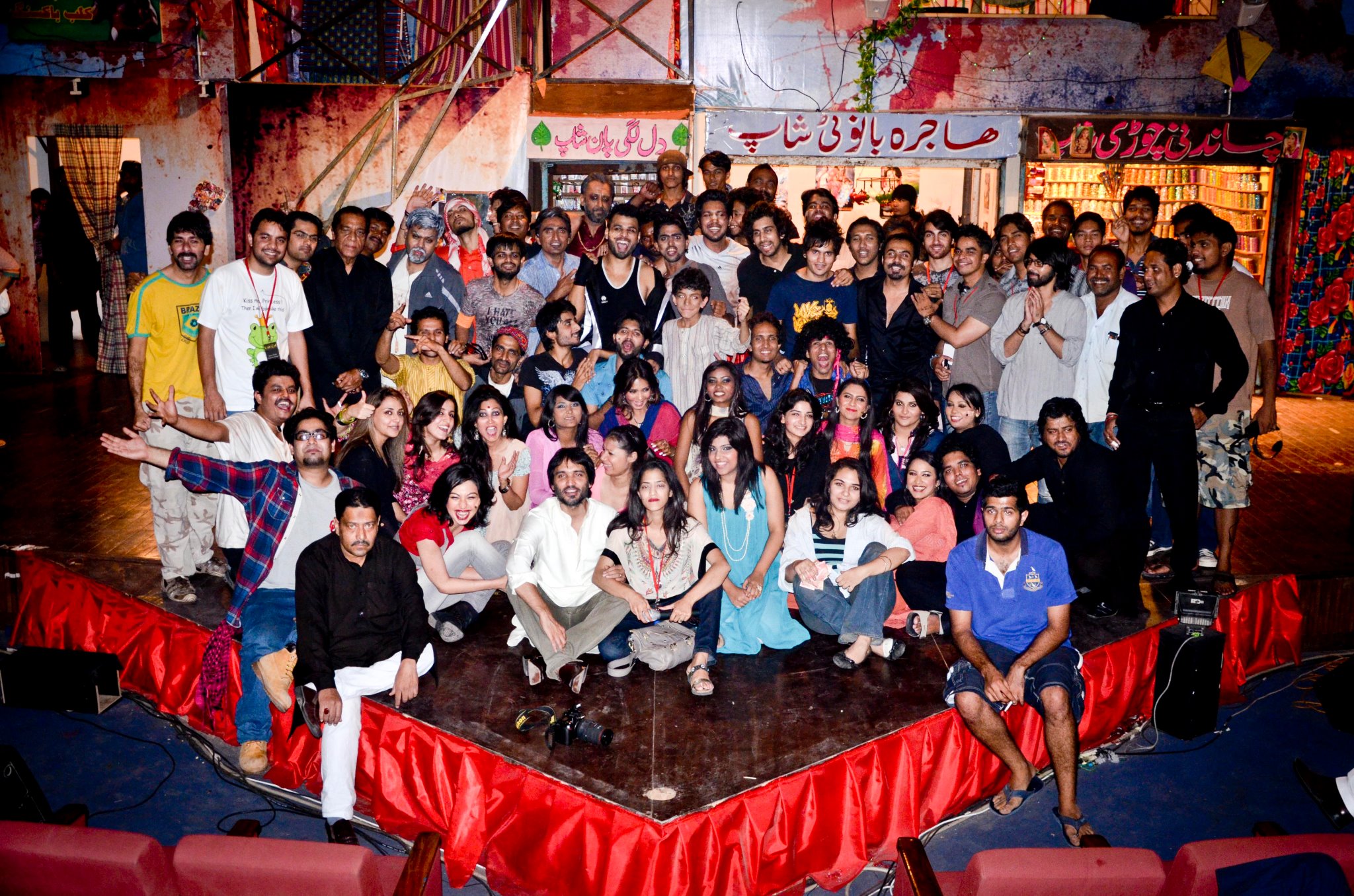 Stage photograph of a packed Arts Council of Pakistan Karachi auditorium in 2011 with dancers, a live band and crew under bright theatrical lighting and the audience seated in the foreground.